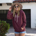 Woman wearing a maroon hoodie with Slant collection design and denim shorts standing in front of a white building with a tiled roof.